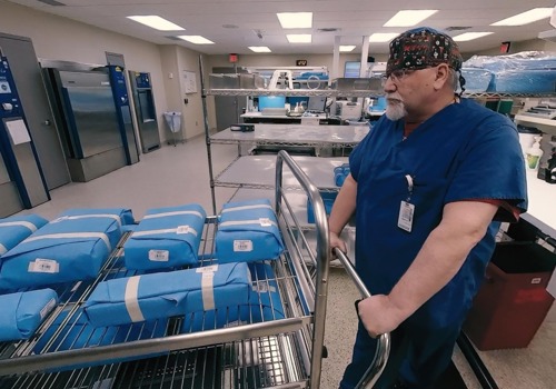 Wrapped surgical instruments are carted into a sterilizing autoclave by a central sterile technician.