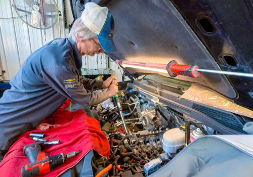 An auto technician uses a torque wrench inside an engine.