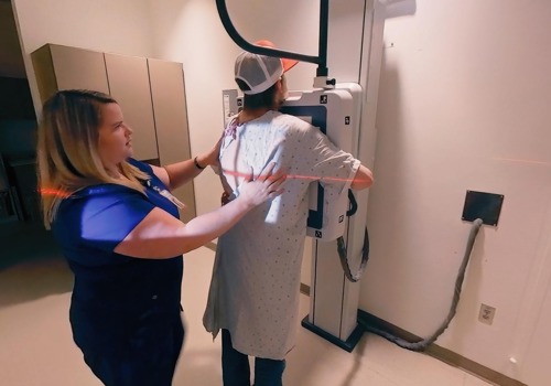 A sonographer helps position a patient for an x-ray image to be taken.