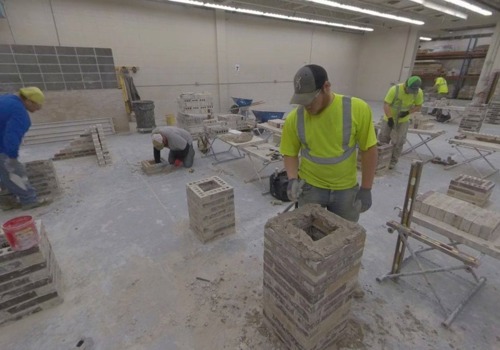 A group of bricklayers-in-training practice laying bricks in an alternating pattern to form a pillar.
